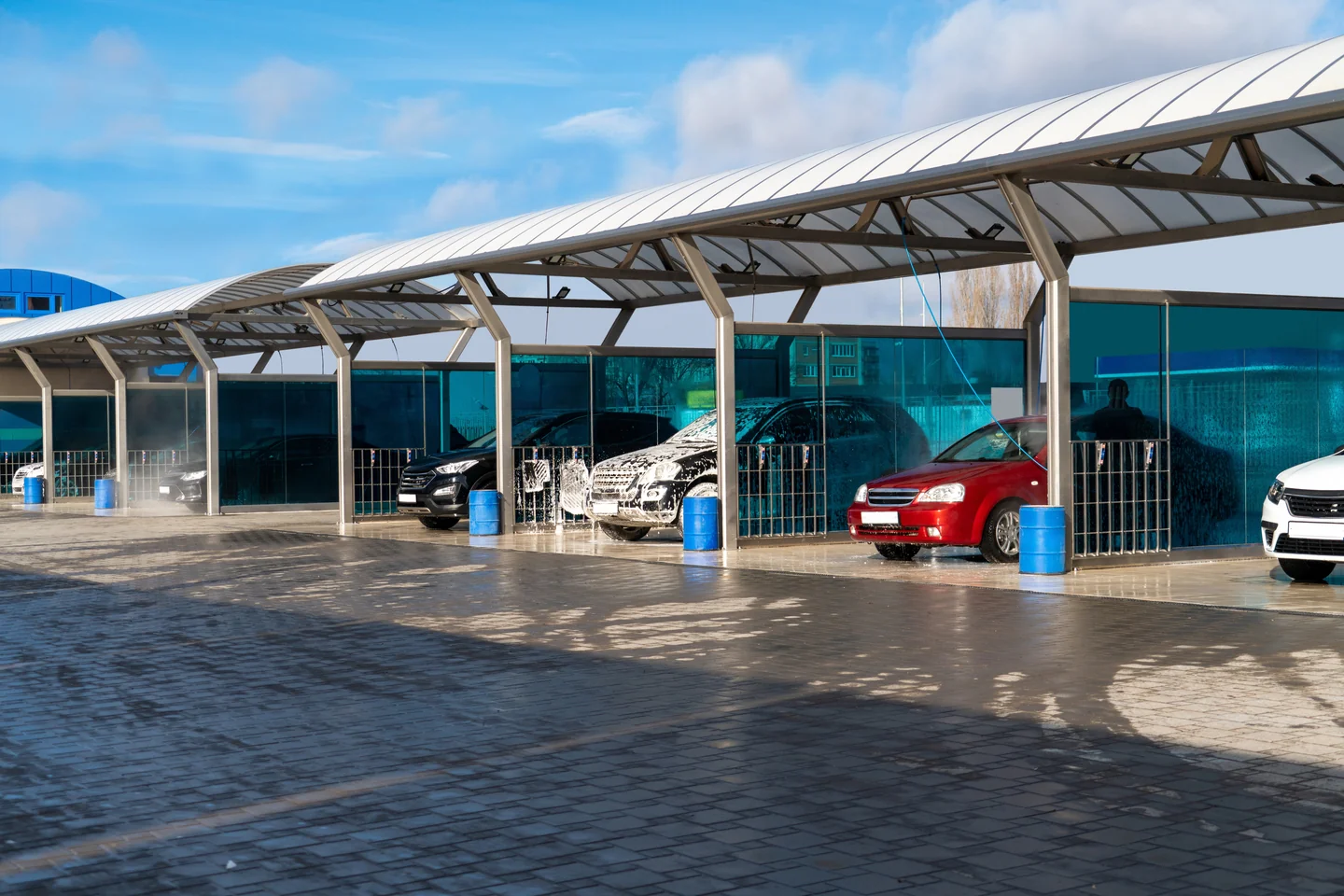 Vehicles under foam in open self-service wash bays beneath a curved canopy