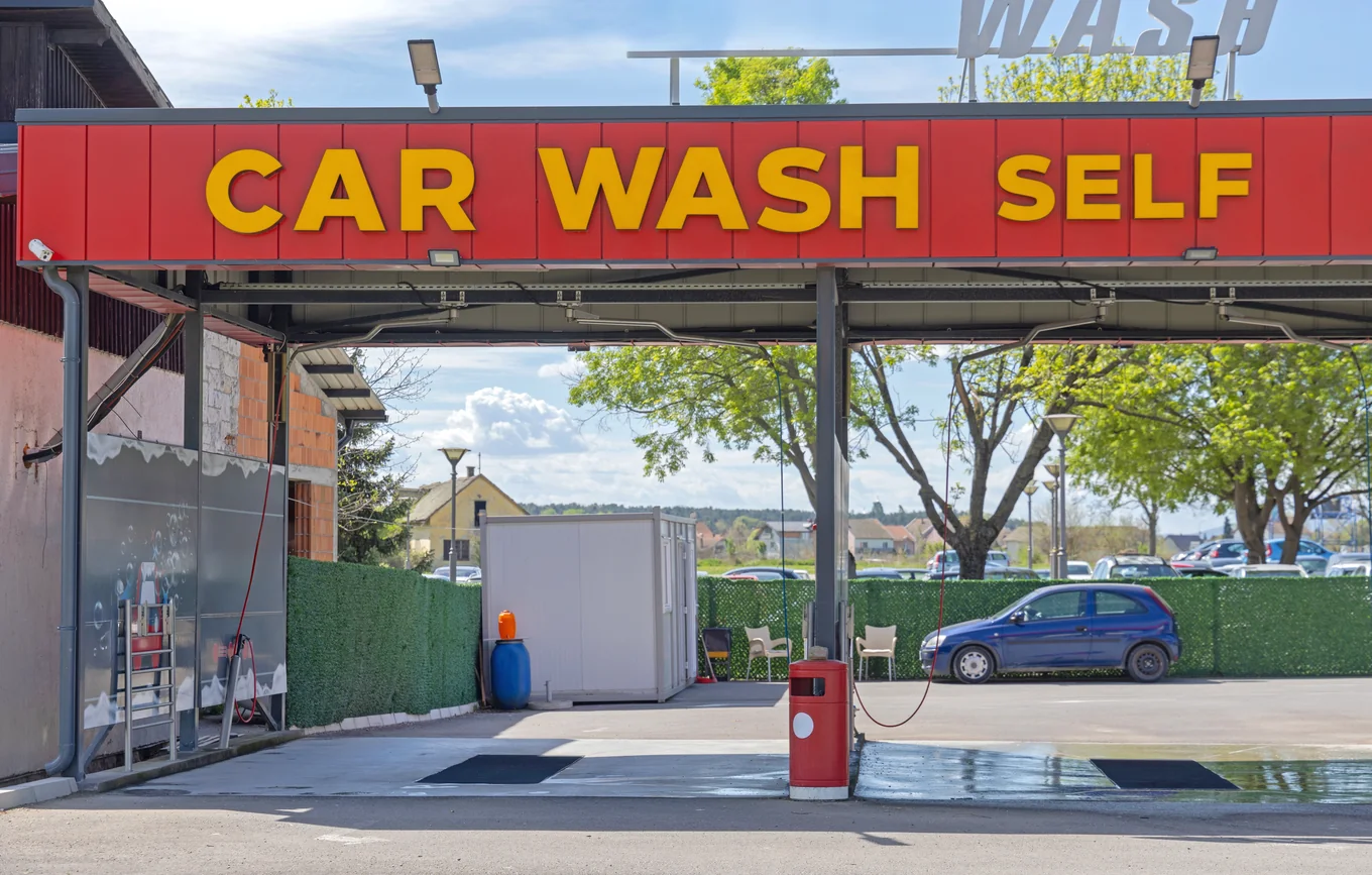 A self-service car wash canopy with open bays and an air pump on the apron