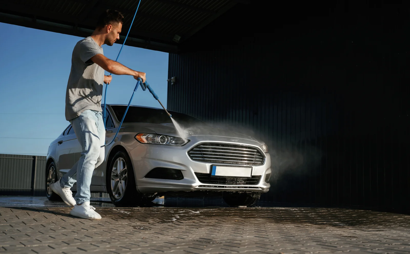 A person rinsing a car with a pressure lance in an open wash bay