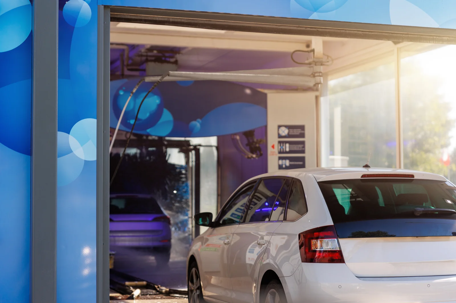A car waiting at the entrance of a lit wash bay with brushes ahead